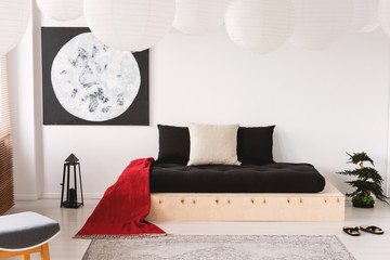 Black sheets and red blanket on wooden bed in bedroom interior with moon poster. Real photo