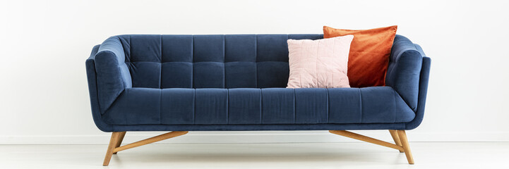 Panorama of navy blue settee with colorful cushions in white living room interior. Real photo
