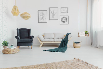 Real photo of a cozy living room interior with grey accents, armchair, sofa and blanket with art...