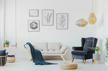Graphics above a wooden couch with pillows, armchair and swing with a plant in a creative living room interior. Real photo