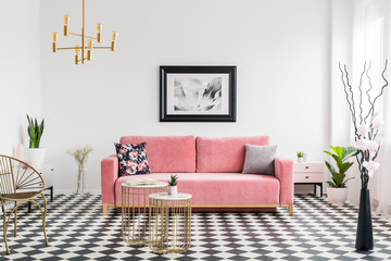 Poster above pink settee in spacious living room interior with plants and gold armchair. Real photo