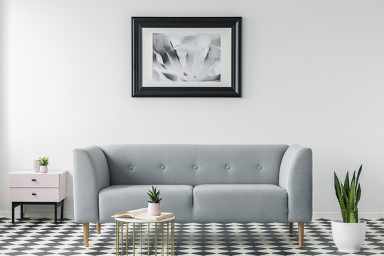 Grey couch between cabinet and plant in simple living room interior with poster and table. Real photo