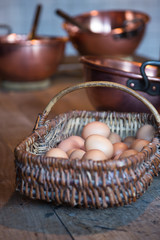 A Basket of Eggs On a Wooden Table with Copper Bowls in the Background in Mont Saint Michel, France