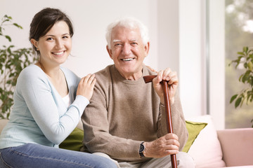 Happy senior man with walking stick and smiling granddaughter