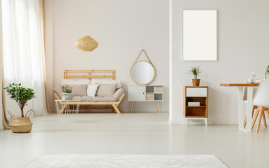 Mockup of white empty poster in bright flat interior with plant near wooden sofa under lamp. Real photo