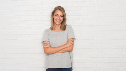 Beautiful young woman over white brick wall happy face smiling with crossed arms looking at the...