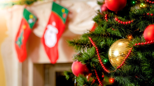Closeup image of golden bauble and colorful lights on Christmas tree against mantelpiece