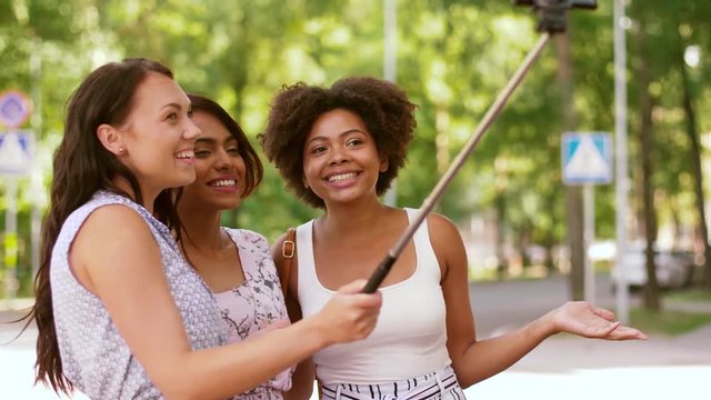 blogging, leisure and technology concept - happy women or bloggers recording video by smartphone and selfie stick in city