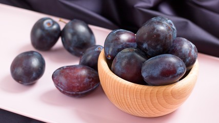 Wooden bowl of purple plums on pink tray