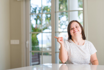 Down syndrome woman at home very happy pointing with hand and finger to the side