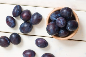 Top down view on ripe purple plums on white wooden table