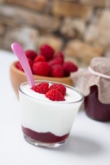Close up on glass cup of fresh yogurt flavored by raspberries with pink spoon