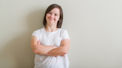 Down syndrome woman standing over wall happy face smiling with crossed arms looking at the camera....