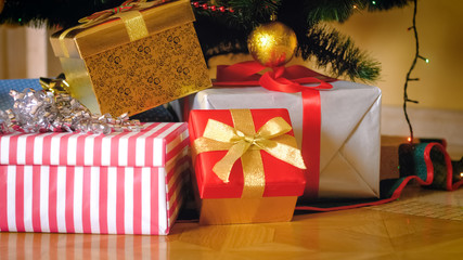 Stack of presents in wrapped in colorful paper lying under Christmas tree