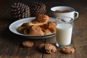 Vaso de leche, plato y taza antigua con bolleria y piñas de pino decorativas.