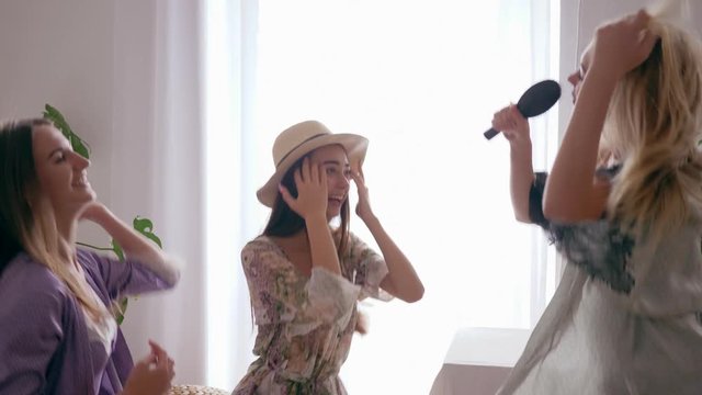 carefree time, girl sing song into comb like a microphon and dance with friends in silk dressing gowns at home