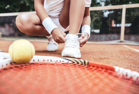 Girl on tennis court in the sport club. Cropped image of a little tennis player. Girl child tying shoelaces on tennis court. Summer activities for children.