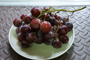 Bunches of fresh ripe red grapes on the dish. Ancient style, a beautiful background with a branch of blue grapes. Red wine grapes. dark grapes, blue grapes, wine grapes