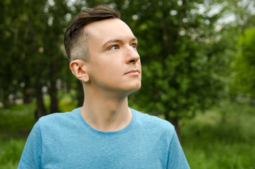 Portrait of young guy looking up, on a green grass and trees background.