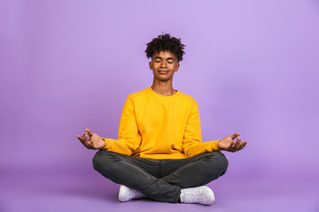 Portrait of relaxed african american boy sitting in lotus pose and meditating with closed eyes, isolated over violet background - Powered by Adobe