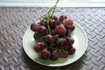 Bunches of fresh ripe red grapes on the dish. Ancient style, a beautiful background with a branch of blue grapes. Red wine grapes. dark grapes, blue grapes, wine grapes