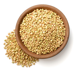 uncooked buckwheat in the wooden plate, isolated on the white background, top view
