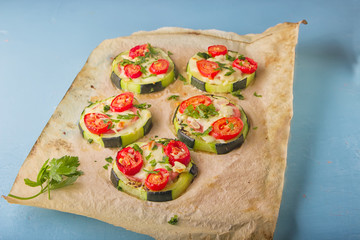 Healthy, nutritious zucchini small round pizza with pepperoni, tomatoes, cheese and parsley on parchment paper on light blue background.
