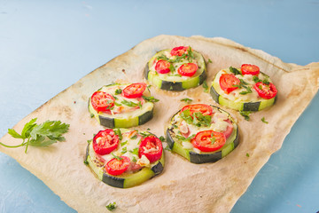 Healthy, nutritious zucchini small round pizza with pepperoni, tomatoes, cheese and parsley on parchment paper on light blue background.
