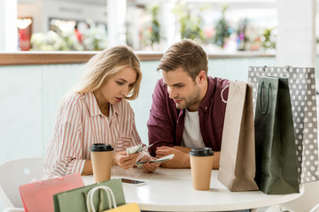 focused young couple counting cash money at table with coffee cups in cafe