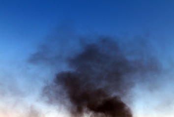 Naklejka na ściany i meble dark smoke pillar on the blue sky background.