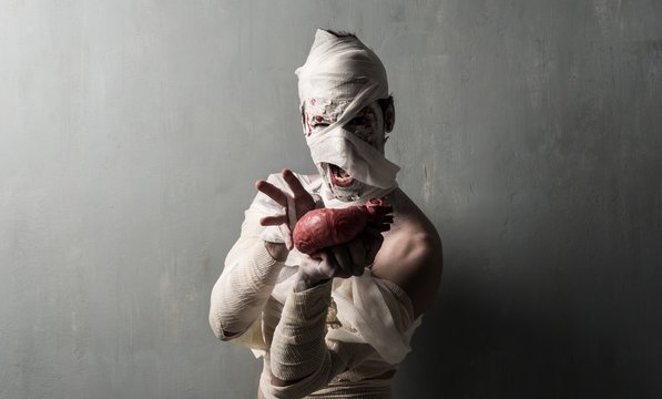 Terrorific Mummy Eating A Heart On Textured Wall Background.  Halloween Holidays