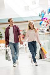 Fototapeta na wymiar happy young couple of shoppers with paper bags walking at shopping mall