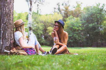 Girls friends sitting in park on blanket talking, drinking 