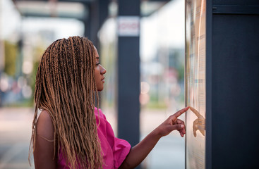 Young African woman checking plan and waiting at city bus stop