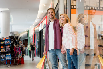  young happy couple with paper bags walking out from store at shopping mall