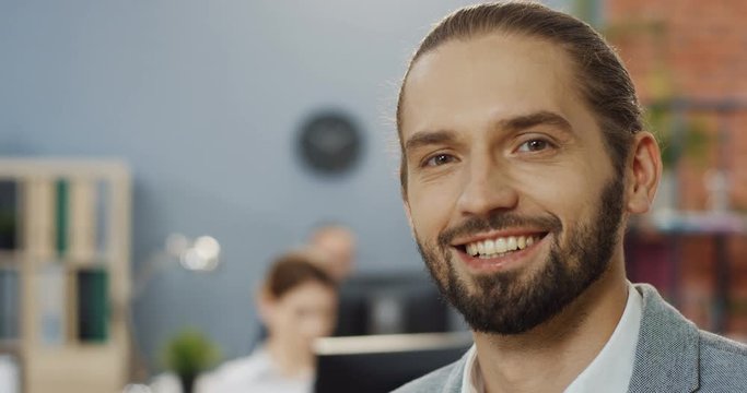 Close up of the attractive young Caucasian man, office worker turning his head to the camera and smiling. Portrait.