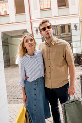 stylish young couple with shopping bags looking at shopwindows on city street