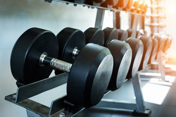 The dumbbell set stacked on rack,at fitness gym,warm light tone,blurry light around