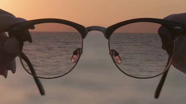 Cinemagraph -Woman's hands hold eyewear, a background of blue seawater. Motion Photo.