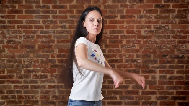 Young cute girl brunette caucasian dancing, brick wall in the background, portrait