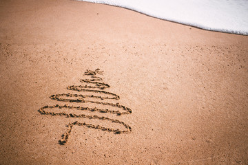 Christmas tree drawn in sand at the beach.