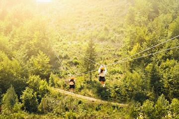 Tourists ride on the Zipline over the forest. Two women in helmets sliding on a zip line in an...