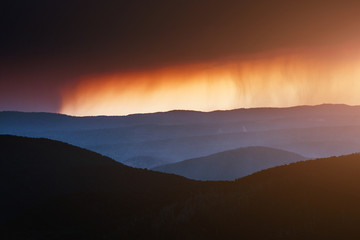 Rain in mountain landscape with clouds at sunset