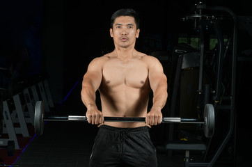 Fototapeta na wymiar Muscular builder man training his body with barbell in Modern fitness center
