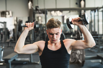 Fototapeta na wymiar Young fit man in gym exercising with dumbbells.