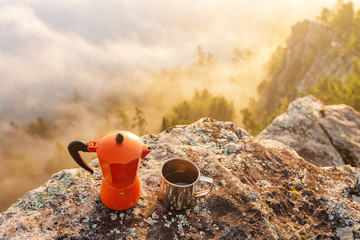 coffeepot and coffee in cup near camping site at foggy mountains background