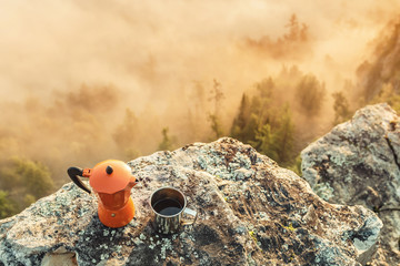 coffeepot and coffee in cup near camping site at foggy mountains background