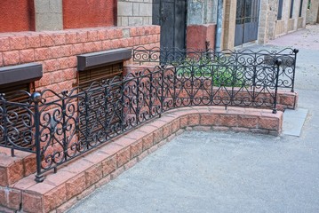 part of the basement with brown windows on the wall and a decorative steel fence with a forged pattern on the asphalt