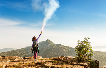 A woman in the wild mountains gives a distress signal SOS using Falsch feuer torch from which comes...