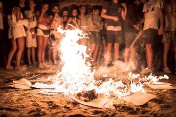 Hoguera de San Juan en la playa con llamas, fuego y personas - obrazy, fototapety, plakaty
